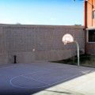 An outdoor basketball court with a single hoop near a brick wall.
