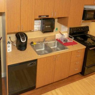 A compact kitchen with wooden cabinets featuring a double sink, coffee maker, dishwasher, stove, and microwave.