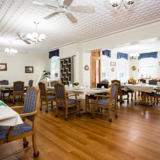 A spacious dining room with neatly arranged tables and chairs, featuring a wooden floor and ceiling fans.