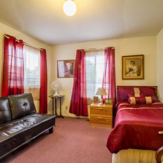 A cozy bedroom with a bed, sofa, and vibrant red curtains.