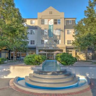 A four-story building with a prominent water fountain in the foreground, surrounded by trees.