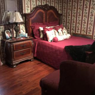 A cozy vintage-style bedroom with a wooden bed frame, matching nightstand, and floral wallpaper.