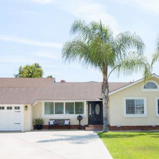 A suburban one-story house with a driveway and palm tree in the front yard.