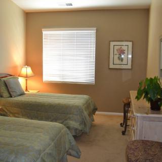 A cozy bedroom with twin beds, a lamp, and a dresser adorned with a plant.