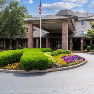 A well-maintained building entrance with landscaped gardens and an American flag flying overhead.
