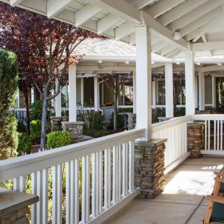A peaceful porch with white railings overlooks a garden with trees.