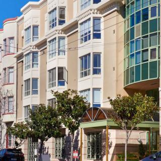 A view of a modern residential building with bay windows and trees lining the sidewalk.