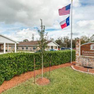 A nursing home entrance with American and Texas flags, surrounded by well-maintained landscaping.