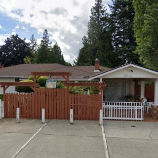 A suburban house with a wooden fence, surrounded by trees under a cloudy sky.