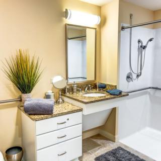A modern bathroom featuring a sink with a mirror, shower area, and decorative plant.