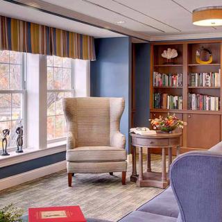 A cozy living room interior featuring an armchair, bookshelves, and a large window.