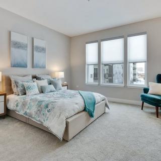 A modern and spacious bedroom with natural light streaming through large windows, featuring elegant decor and comfortable furnishings.
