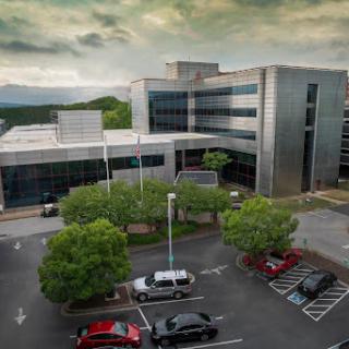 A modern office building surrounded by greenery and a parking area on a cloudy day.
