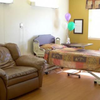 A hospital room with a bed, balloons, and a chair near a window.