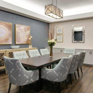 A modern dining room with elegant decor, featuring a long table surrounded by patterned chairs, adorned with artwork and a central chandelier.