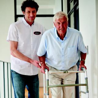 A caregiver assisting an elderly man using a walker.
