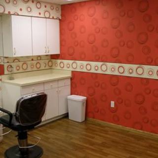 A salon room with red patterned wallpaper, a styling chair, cabinets, and wood flooring.