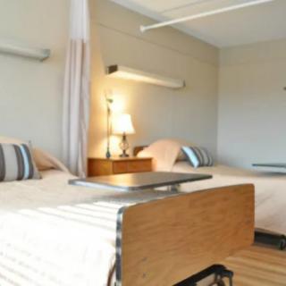 A hospital room with two beds, equipped with bedside tables and medical equipment.