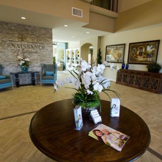 A well-decorated lobby featuring a central table with a floral arrangement and brochures, surrounded by comfortable seating and artwork on the walls.