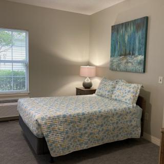 A cozy bedroom with a neatly made bed, lamp on the nightstand, and artwork on the wall.