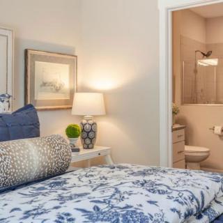 A cozy bedroom with elegant decor, including a lamp and artwork, adjoins a small bathroom.