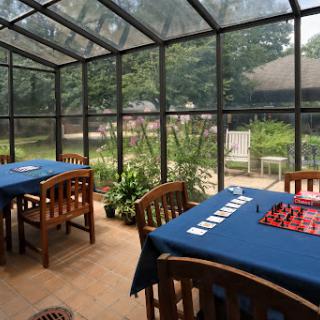A serene sunroom featuring wooden tables and chairs, with a lush garden view through glass walls.