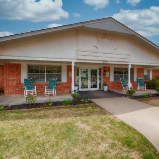 A welcoming entrance to a brick building with a porch and well-kept landscaping.