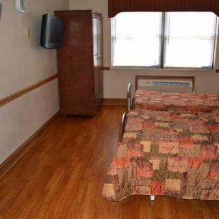 A simple hotel room with a bed, television, and wooden flooring.