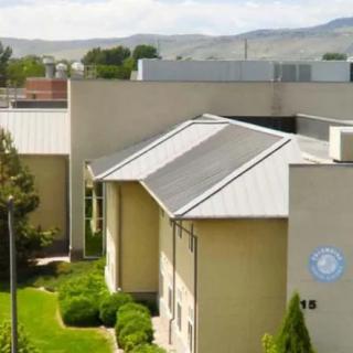 A modern building surrounded by greenery with mountains in the background.