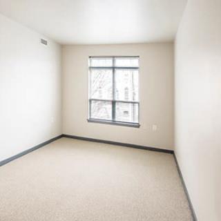 An empty room with beige walls, a carpeted floor, and a window letting in natural light.
