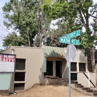 A small building with a street sign at the corner, surrounded by trees.