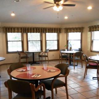 A cozy dining area with several round tables and chairs, well-lit by natural light through large windows.