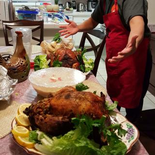 A person in a red apron presenting a table set with a roasted turkey and various dishes.