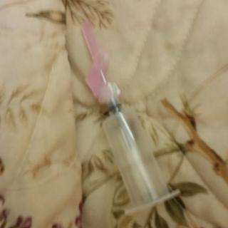 A syringe with a pink needle cap lying on a patterned surface.