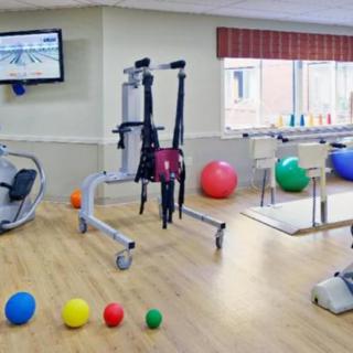 A rehabilitation room equipped with gym equipment, including exercise balls and parallel bars.