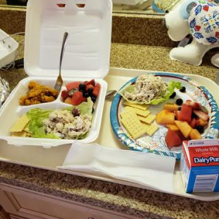A colorful and nutritious lunch featuring a chicken salad with fresh fruits and a side of assorted melon.