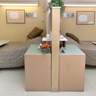 A hospital room with two beds separated by a partition, each equipped with medical equipment and furnishings for patient care.
