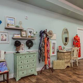 A vintage boutique interior featuring clothing, hats, and accessories displayed on antique furniture.
