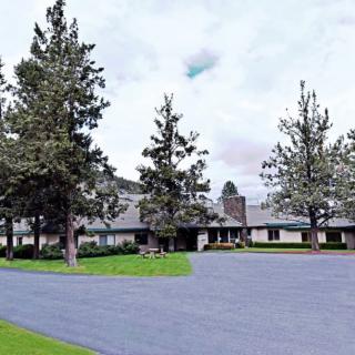 A large house with a long driveway, surrounded by tall trees under a cloudy sky.
