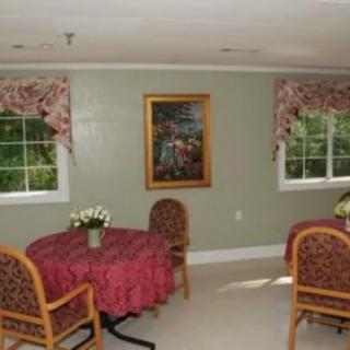 A cozy dining area with tables and chairs, decorated with floral arrangements and a painting on the wall.