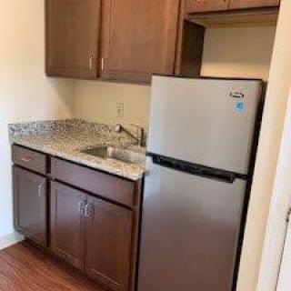 A compact kitchen with wooden cabinets, a sink, and a stainless steel refrigerator.