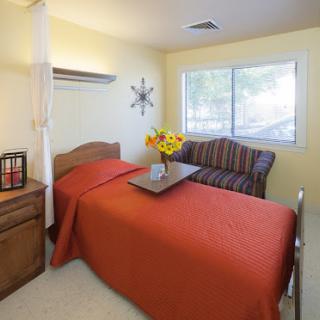 A cozy and well-lit bedroom featuring an orange bedspread, a comfortable sofa, and vibrant flowers.