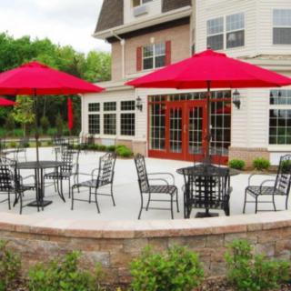 A patio with outdoor seating and red umbrellas in front of a brick building.