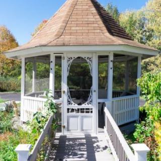 A charming wooden gazebo set amidst a lush garden with a pathway leading to its entrance.