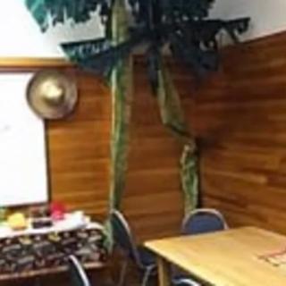 A cozy room with wooden walls, featuring a table, chairs, a decorative palm tree, and a hat on the wall.