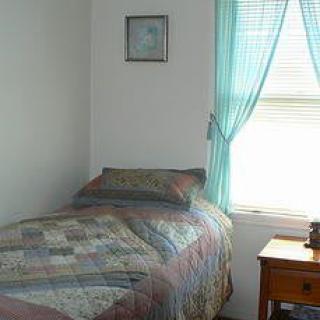 A simple bedroom with a single bed and a nightstand near a window covered with sheer curtains.