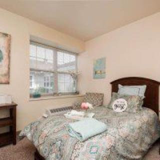 A cozy bedroom with a single bed, decorated with patterned bedding and soft pillows, featuring a large window allowing natural light to fill the space.