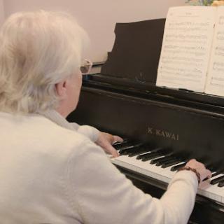 An elderly musician playing the piano while reading sheet music.