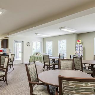 A spacious community dining area with several tables and chairs, well-lit by natural light through multiple windows.