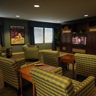 A cozy living room with several armchairs, a television, and a framed poster on the wall.